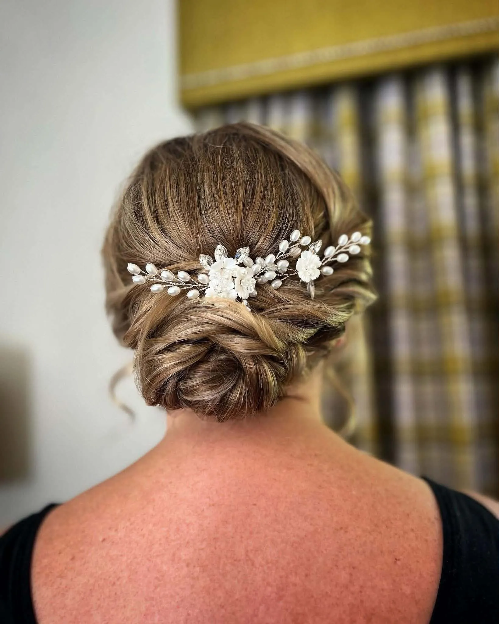 Soft low bridal updo in blonde hair with a white flower and pearl comb set across the back