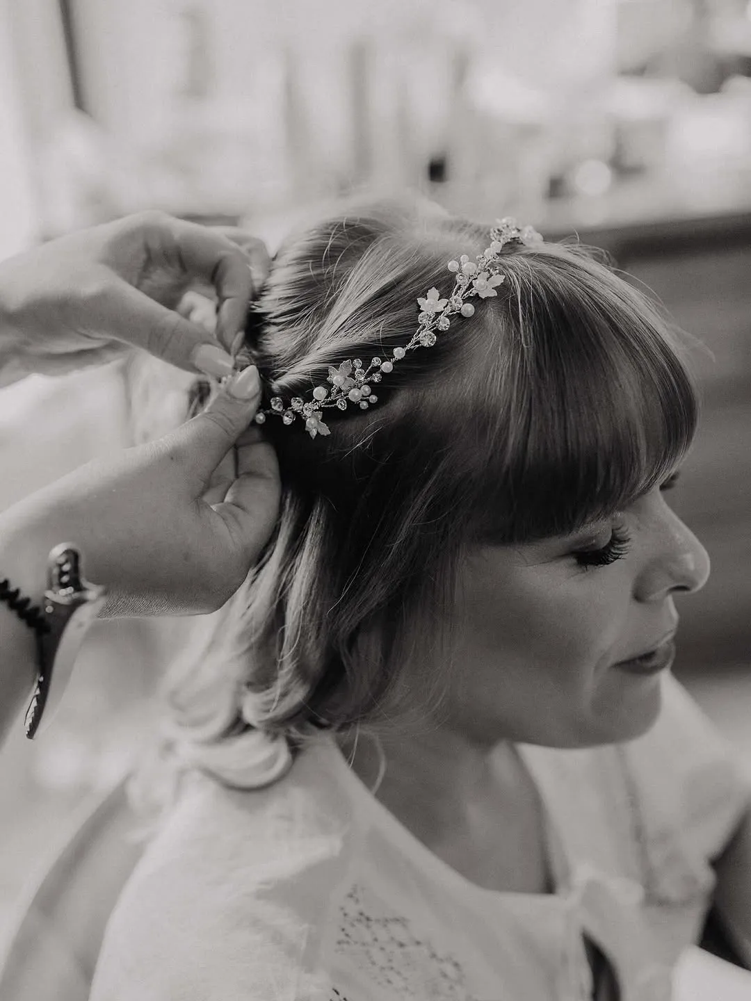 Hands pinning a pearl and crystal hair vine into a bride's half-up style.