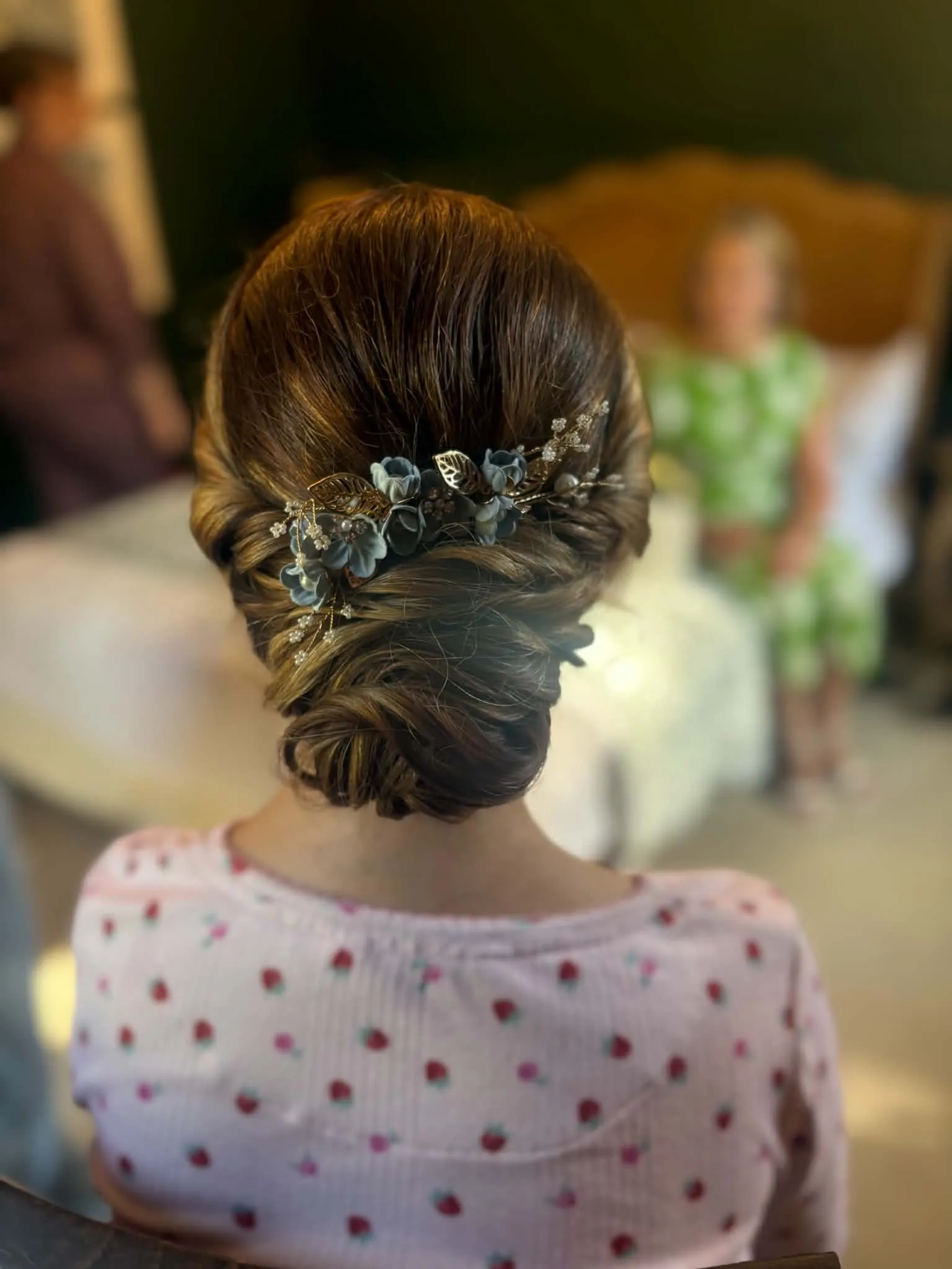 Smooth low chignon in brown hair with a blue-grey flower vine wrapped across it